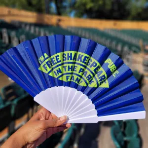 Hand showcasing I'm a Free Shakespeare in the Park blue and green folding fan.