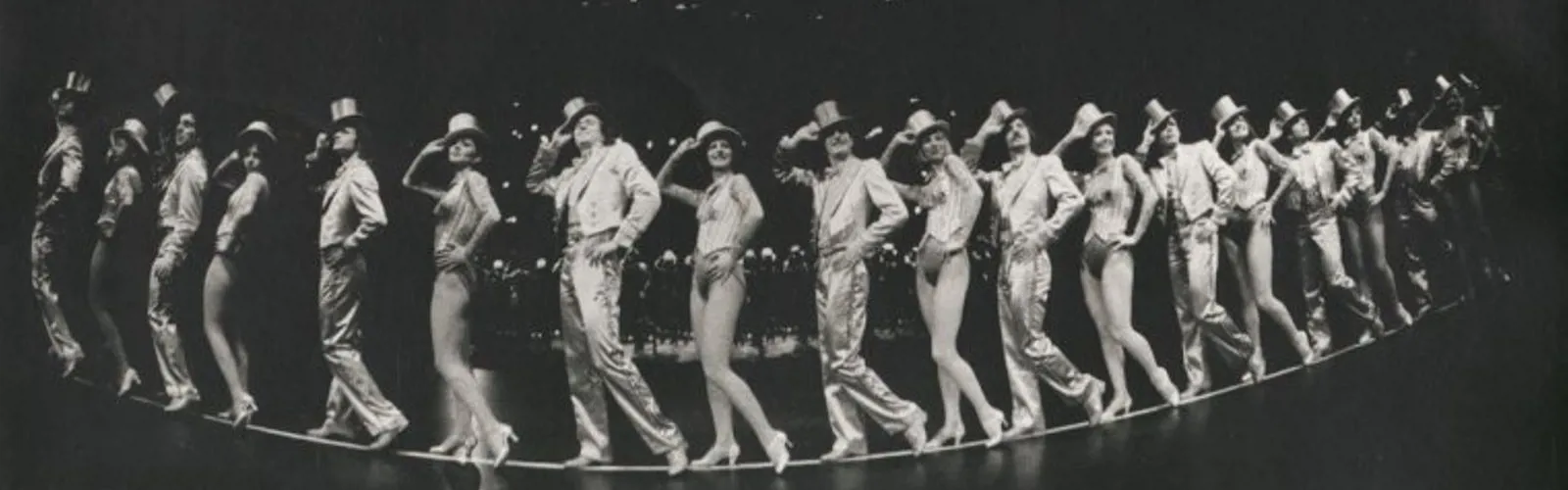 Sixteen members from the original cast of A CHORUS LINE standing with their hands on their top hats.